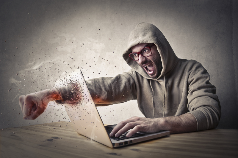 Angry man putting his fist through laptop computer screen