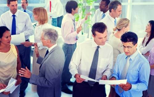 A group of people in business attire grouping up for discussions while holding papers